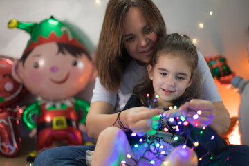 Cute little girl interacting interestedly with the Christmas lights, sitting on her mother's lap...