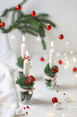 Christmas decoration. Candles in a glass jars decorated with fir and red berries on white table.