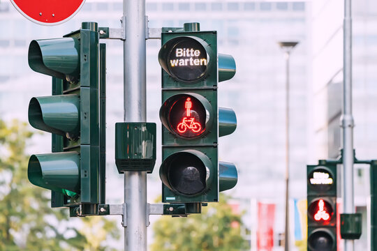 Red forbidding traffic light for pedestrians and cyclists and the inscription - please wait in German. accidents and traffic rules