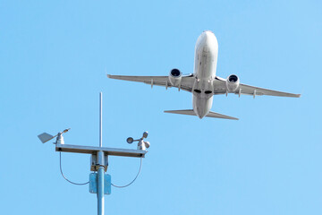 Taking off passenger plane in blue sky during good weather over weather vane and anemometer.