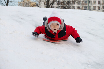 The boy climbs down on a sledge on a hill