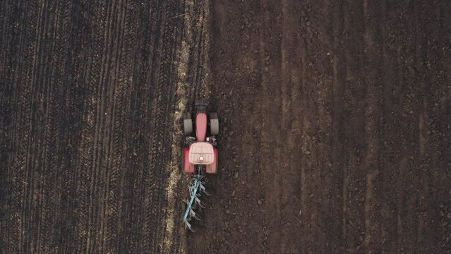 Tractor is plowing in spring - sowing season. The tractor goes through the field and the pulling plow - aerial drone shot. Cultivation of arable land in Ukraine.