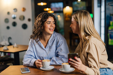 Two young business women sit at the cafe and talk