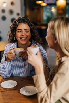 Two female friends are sitting at a cafe and drinking coffee