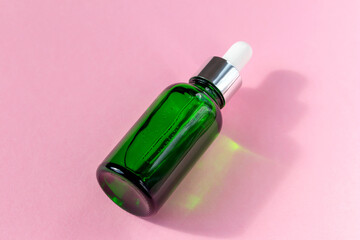 Green cosmetic bottle on pink background