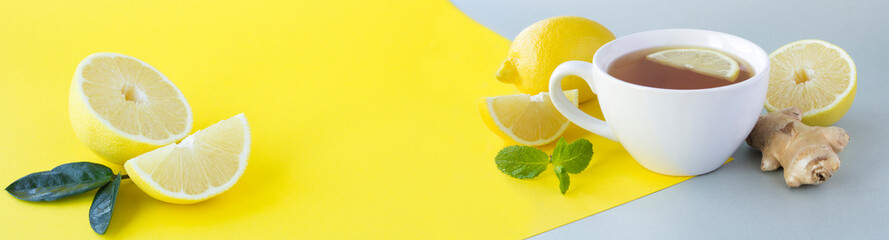 Tea with lemon and ginger in the white cup on the gray and yellow background. Copy space.