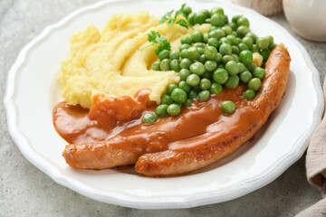 Bangers and mash. Grilled sausages with mash potato and green pea on white plate on grey background. Traditional dish of Great Britain and Ireland. BBQ beef sausages. Top view.