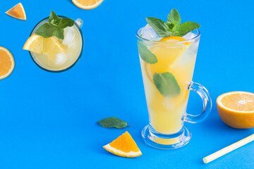 Orange drink or lemonade with mint and ice in the drinking glass on the blue background. Close-up. Copy space.