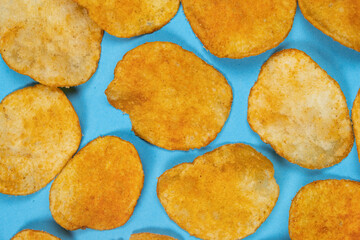 Delicious crispy potato chips with spices on a blue background, top view