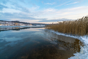 A mirror image of the sky and the shore with a snow cover on the reservoir .