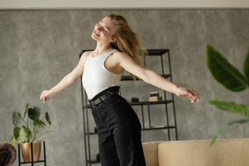 cheerful blonde woman dancing with closed eyes while having fun at home.