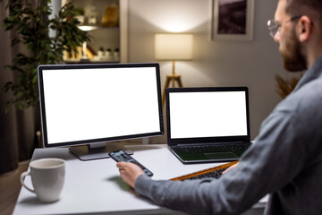 Male employee working with laptop and blank template on display, looking at isolated mockup screen. Using white copyspace background on laptop at home desk.