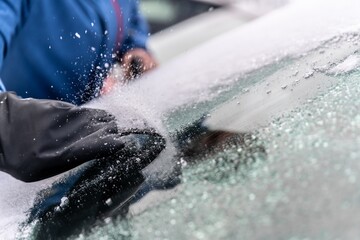 man uses ice scrapers to thaw an ice-covered car windshield