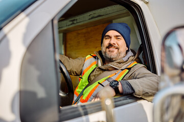 Happy truck driver sitting in vehicle cabin and looking at camera through side widnow.