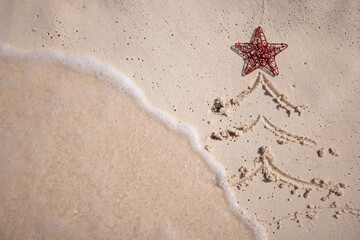 Christmas tree drawn on the sandy beach with red star and the wave is coming close.