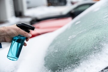 Man uses a bottle of de-icer to defrost the ice-covered windshield of his car - 553847560