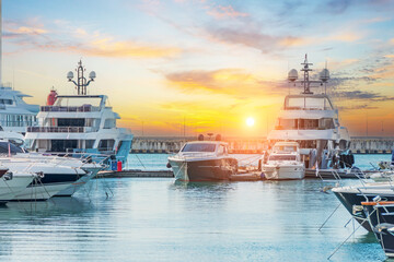 Marine parking of modern motor boats and blue water. Luxury yachts docked in sea port at sunset. Tranquility, relaxation and fashionable vacation.