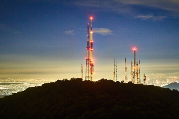 antenna in top of mountain with bright lights of city in the background, night in sierra de guadalupe, state of mexico 