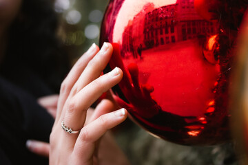 A young woman, girl reaches out and touches with a hand a red glass ball, Christmas tree toy. New...