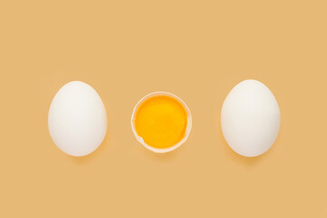 Whole chicken Eggs and cracked half with yolk on yellow background. Minimalism