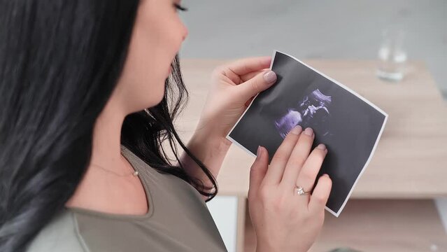motherhood, a tender pregnant woman is happy to look at an ultrasound photo in anticipation of a baby, close-up