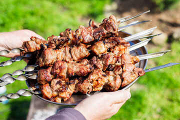 tray with barbecue on iron skewers in the hands of a man on the street. Delicious picnic lunch
