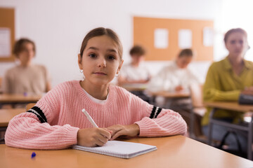 Young girl sitting at desk in classroom and looking at camera.