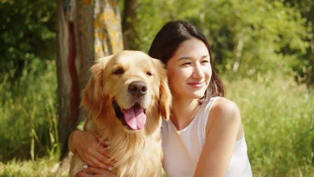 Woman petting golden retriever, young pet owner portrait. Female handler stroking labrador close-up, walking together in forest. Happy dog puppy. 