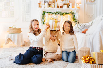 two girls and a little boy with gift in the box r in a room with Christmas decor