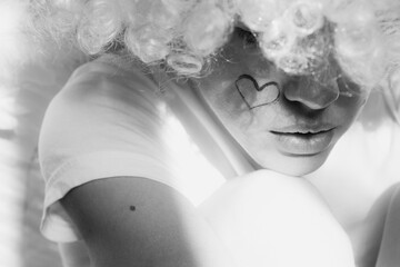 Girl dressed as an angel with wings and curly hair with a painted heart on her cheek on an isolated...