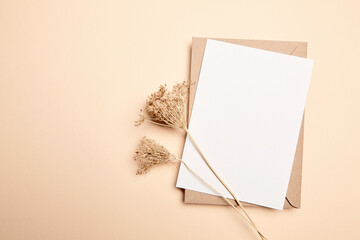 Holiday greeting card mockup with dry grass on beige background, top view, flat lay. White wedding invitation card