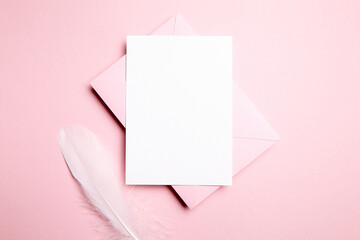 Obraz na płótnie Canvas Holiday greeting card mockup with pink envelope and white feather on light pink background, top view, flat lay. Blank wedding invitation or Valentine Day letter, empty card