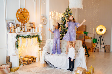 two girls and a little boy play with pillows in a room with Christmas decor.