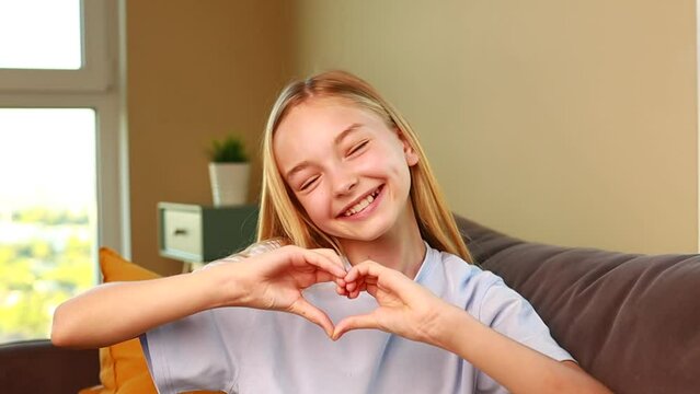 happy little girl showing heart shape gesture in cozy living room at home
