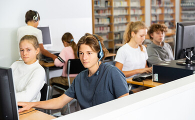 Obraz premium Portrait of a fifteen-year-old schoolboy in headphones, studying at a computer in the classroom at a informatics lesson