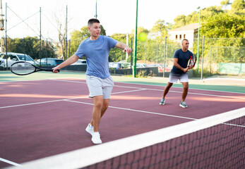 Obraz premium Young teenage tennis player training on court with male partner. Boy using racket to hit ball.
