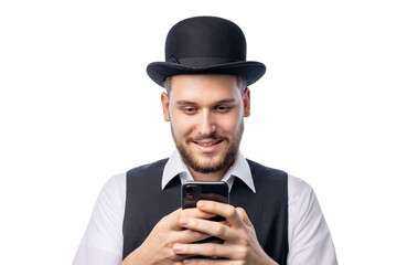 Man in funny old-fashioned hat, black waist and white shirt holding smartphone and smiling isolated on white background