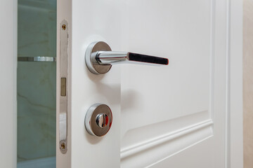 Modern metal door handle on white wooden door in interior. Knob close-up elements. Door handle, fittings for interior design