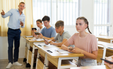 Interested teen girl student using smartphone while studying in college with group of classmates..