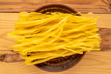 Homemade raw noodles with clay plate on wooden table, macro, top view.