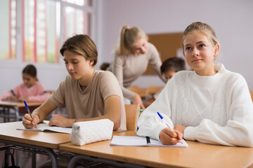 Fototapeta premium Portrait of teenage school girl and boy sitting together in classroom during lesson in secondary school