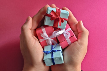 blue and pink wrapped gifts with ribbon in male palm over pink background
