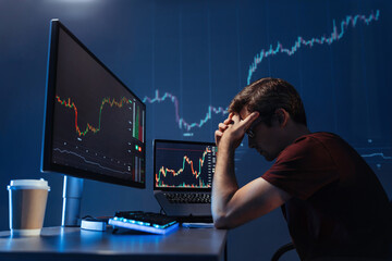 Side view of depressed thoughtful male crypto investor holding head in hands in front of computer...