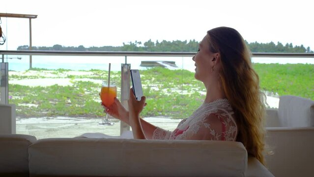 Woman with a mobile phone and a cocktail. Happy female on Maldives. 