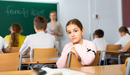 Portrait of unhappy kid girl studying in classroom at secondary school, learning lessons