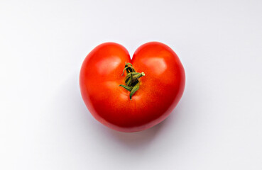 Wonky shaped red tomato in the shape of a heart shot from above on a white surface.