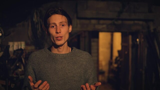 Sad man talking on camera staying outside night in vintage place, old basement background.