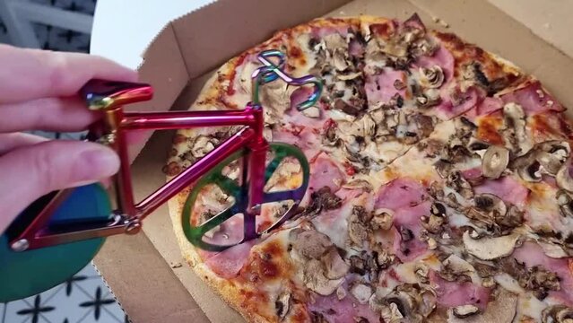 woman hand cutting delicious pizza slices in carton box on table, bicycle pizza cutter knife on cheese in cardboard, fast food delivery service 