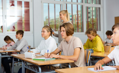Teenagers sitting at desks in classroom during lesson and doing tasks.