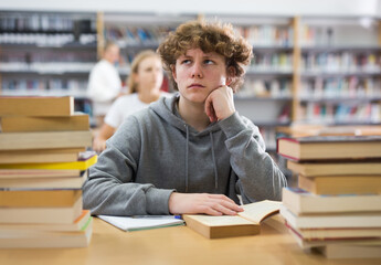 Bored teenage boy trying to prepare for exam in school library